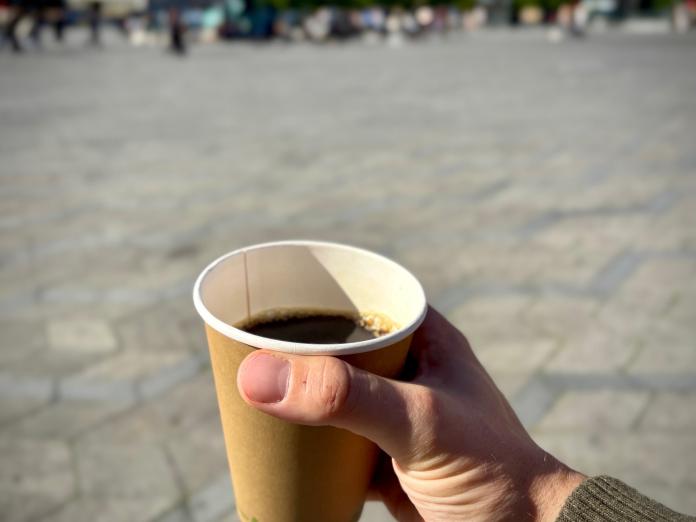 hånd holder kop med kaffe i papkrus