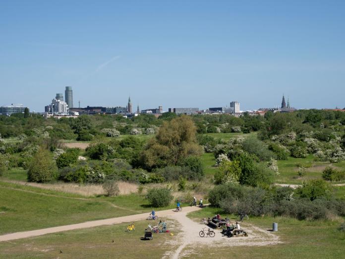 Amager Fælled. Cykler og mennesker ved højene med byens skyline i baggrunden.
