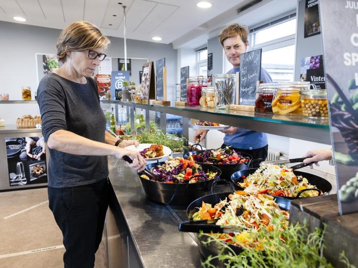 Personer tager mad fra en buffet i en moderne kantine.